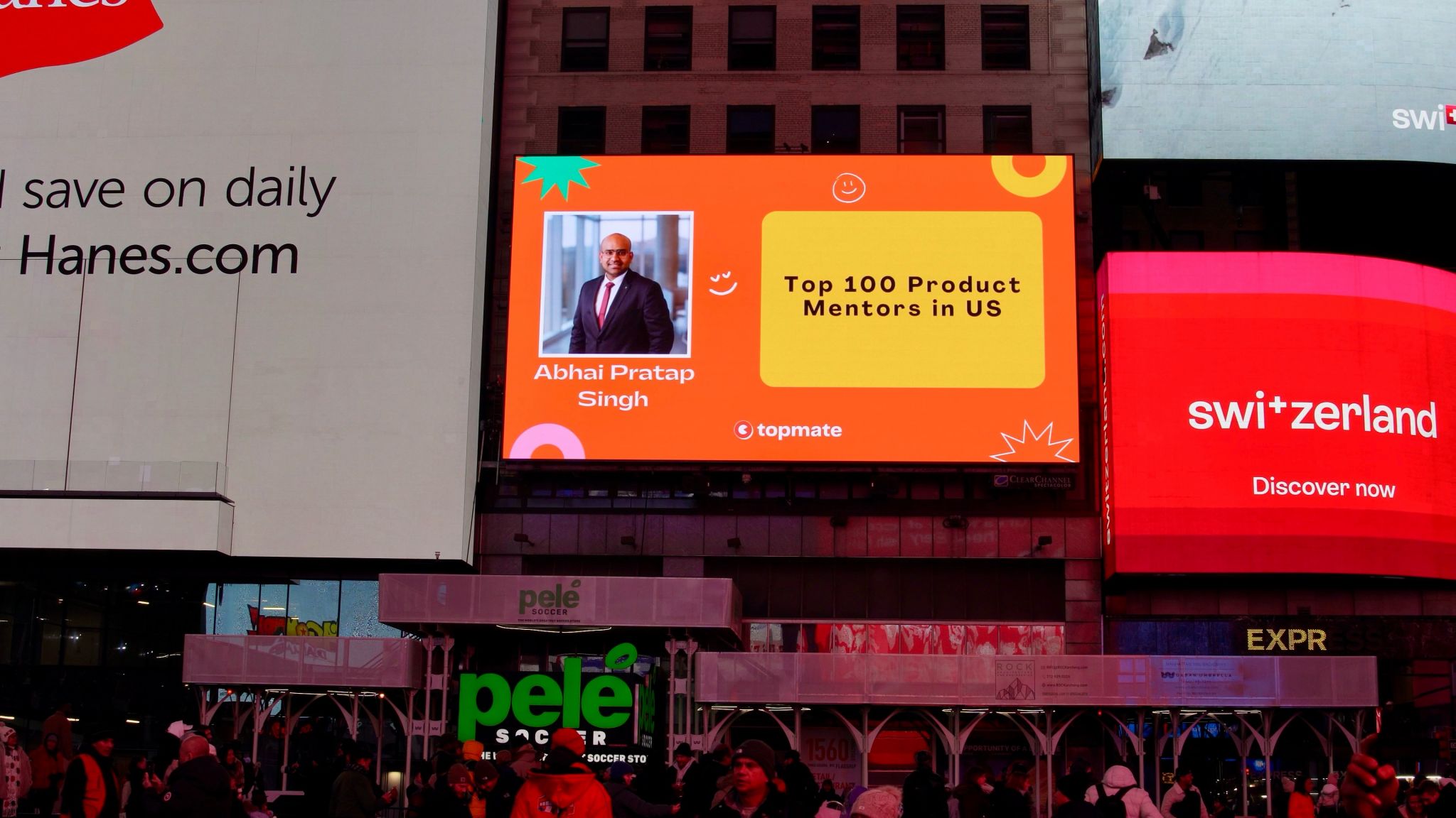 A digital billboard in Times Square displays a photo of a man with text reading "Abhai Pratap Singh: Top 100 Product Mentors in US" above street-level advertisements.