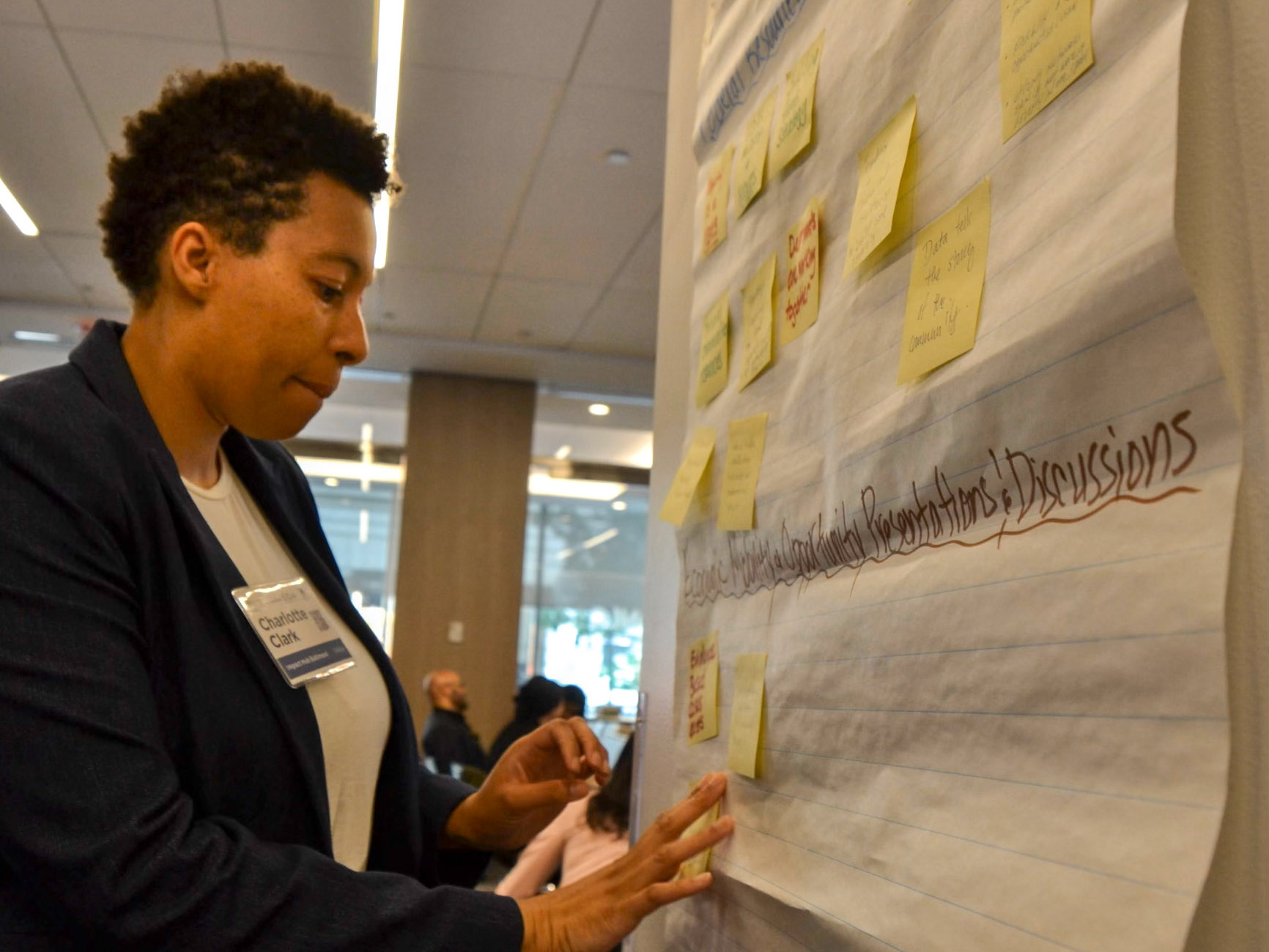 A person places sticky notes on a large paper pad during a group discussion in a conference room setting.