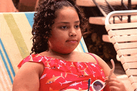 A girl in a red shark-print swimsuit sits on a lounge chair, puts on sunglasses, and looks unimpressed.