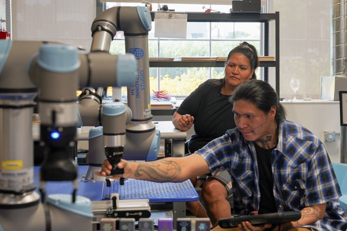 Two people operate a robotic arm in a lab setting, focusing on programming or adjusting the machine amidst technical equipment.