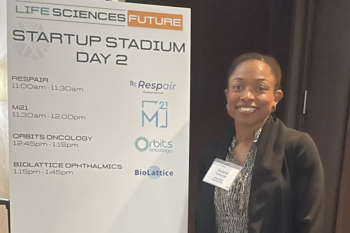 A woman stands next to a sign listing the Day 2 schedule for a Life Sciences Future Startup Stadium event, featuring presentations by Respair, M21, Orbits Oncology, and BioLattice.