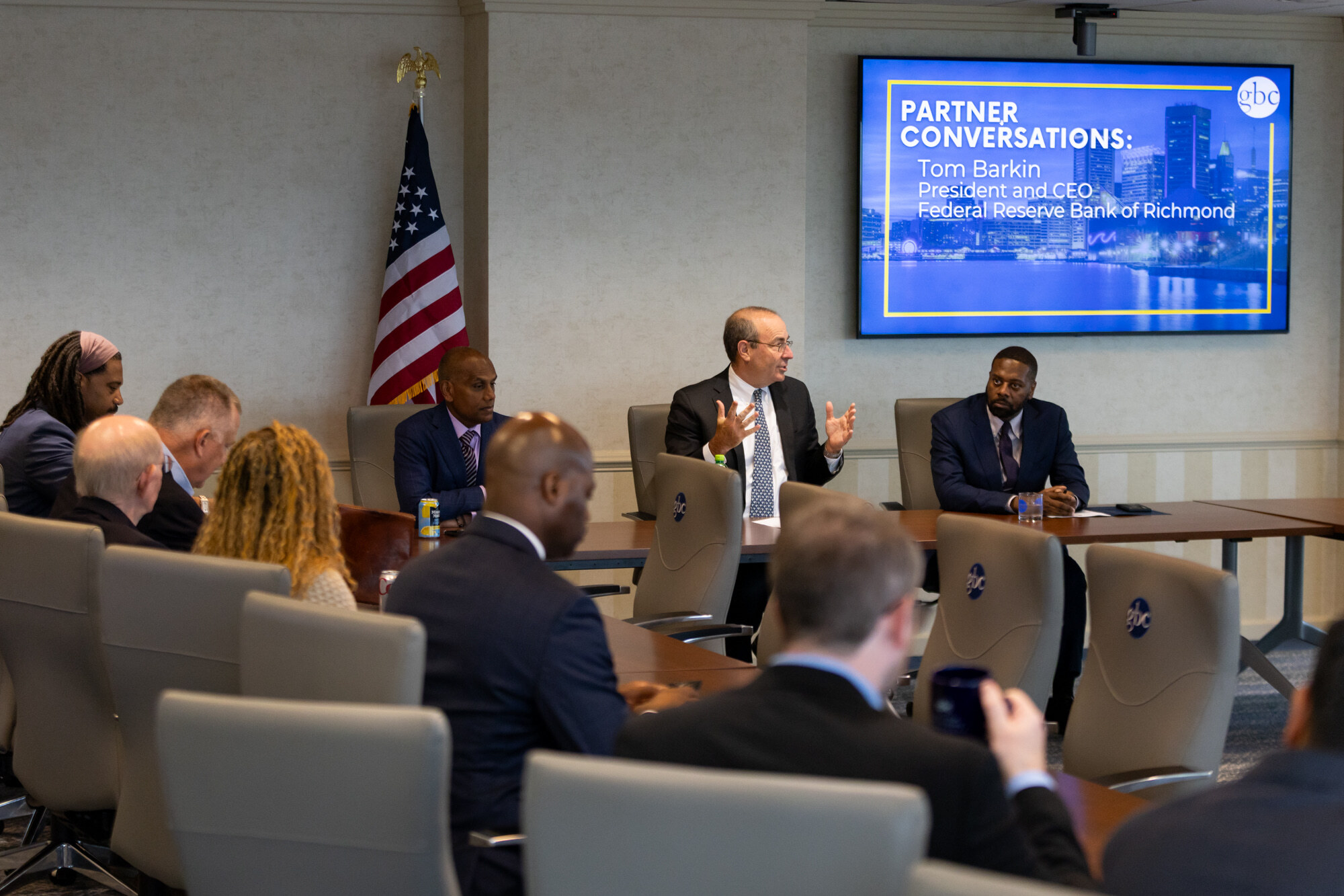 A group of professionals attend a meeting with Tom Barkin, President and CEO of the Federal Reserve Bank of Richmond, who speaks while seated at a conference table.