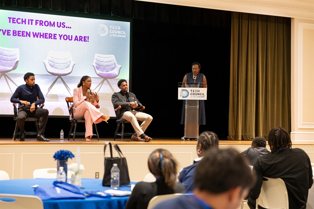 Four panelists participate in a discussion on stage at a Tech Council event, with an audience seated and listening attentively.