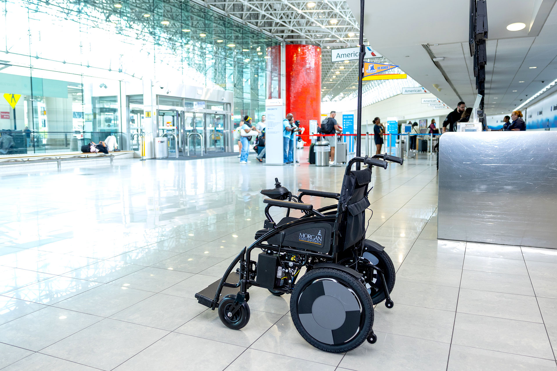 A wheelchair sits unoccupied in a spacious, modern airport terminal near check-in counters and large glass windows.