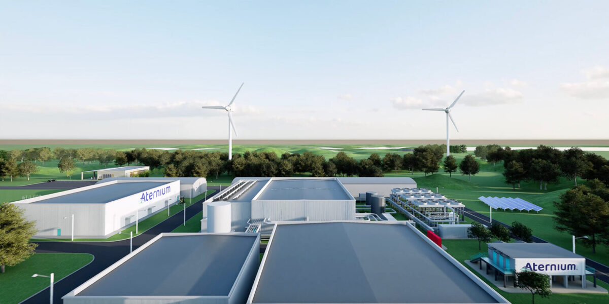 Aerial view of an industrial facility with multiple buildings labeled "Aternium," surrounded by trees, wind turbines, green fields, and a clear sky.