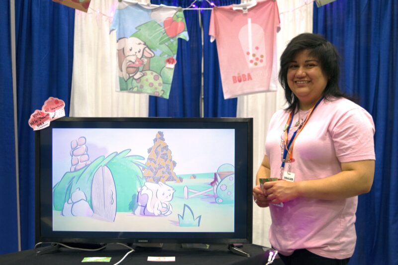 A woman wearing a pink shirt stands next to a tv with a video game displayed.
