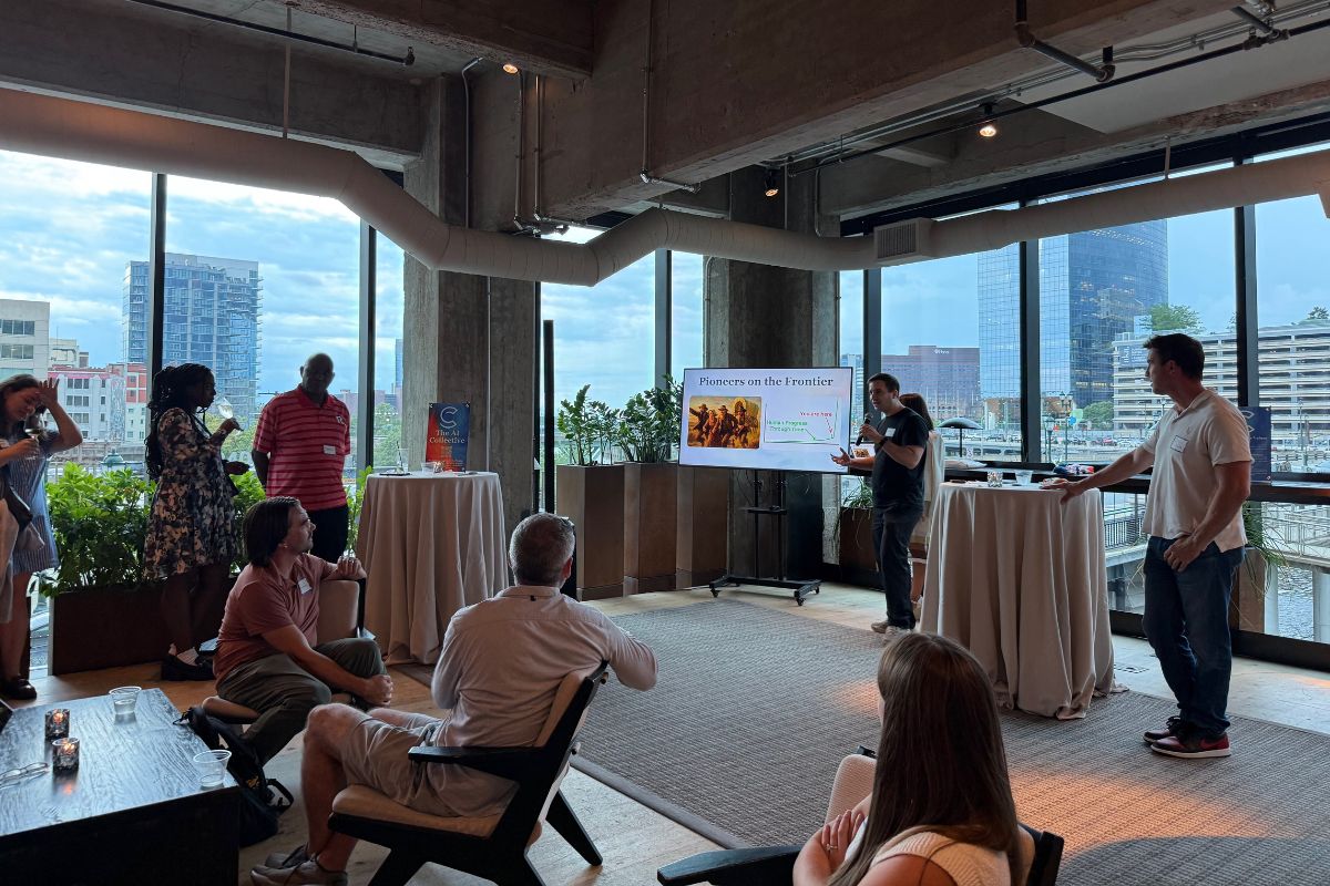 A presenter speaks to a small audience in a modern room with large windows, displaying a slide titled "Pistores on the Frontier" on a screen.
