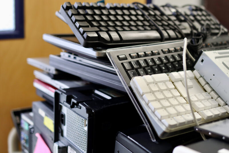 A pile of old keyboards, laptops, and computer towers stacked together, suggesting electronic waste or discarded computer equipment.