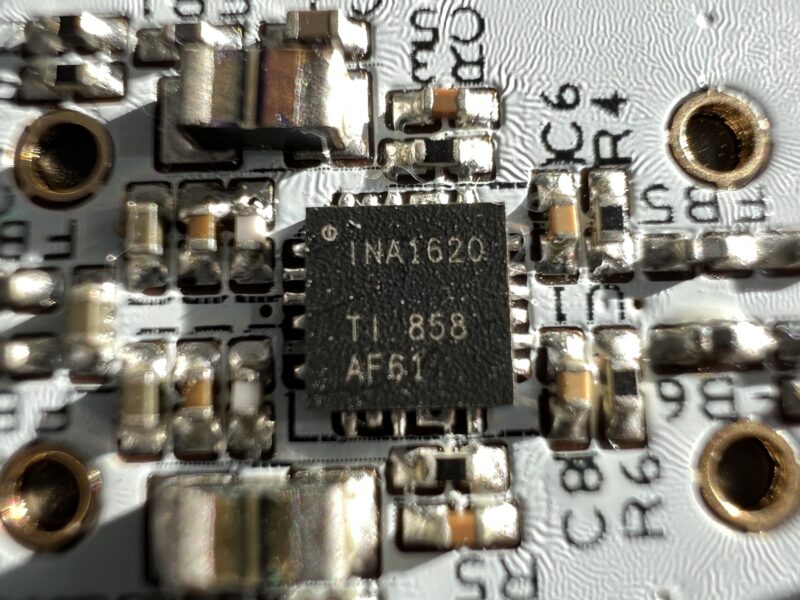 Close-up view of a circuit board featuring an INA1620 TI 858 AF61 integrated circuit chip with visible soldered connections and printed components.