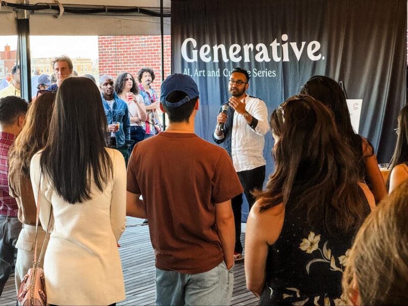 A man speaks into a microphone to an audience at an indoor event titled “Generative. AI, Art, and Culture Series.” People stand facing the speaker, listening attentively.