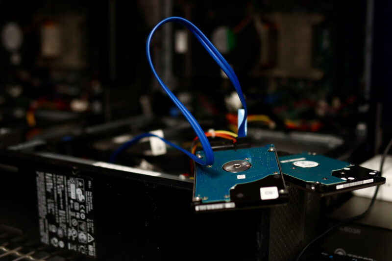 Two hard disk drives connected by blue cables rest on an open computer case with visible internal components and power supply.