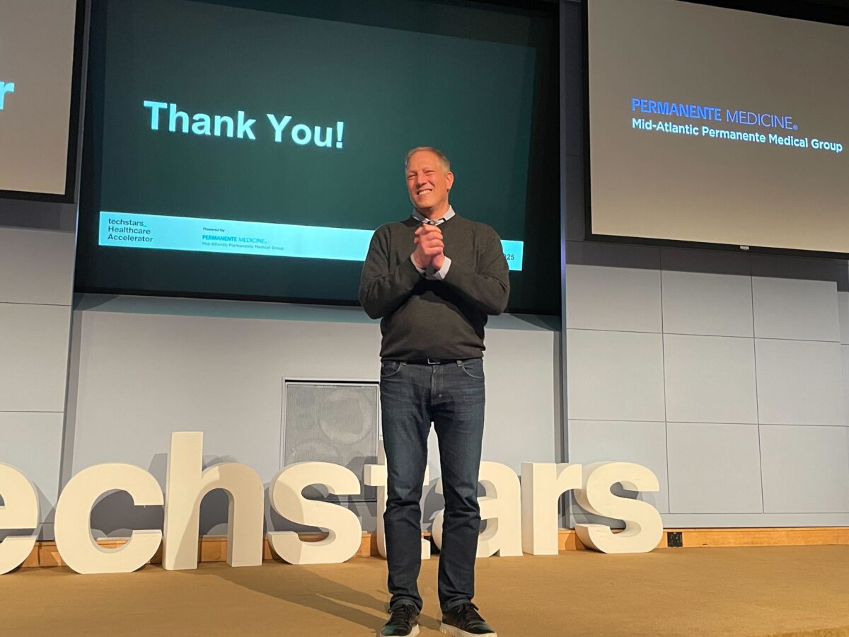 A man stands on stage smiling, with a "Thank You!" slide displayed behind him and large white letters spelling "techstars" on the floor.