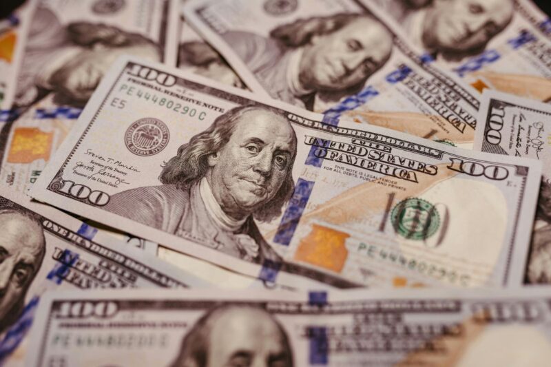 A pile of United States one hundred dollar bills featuring Benjamin Franklin's portrait.