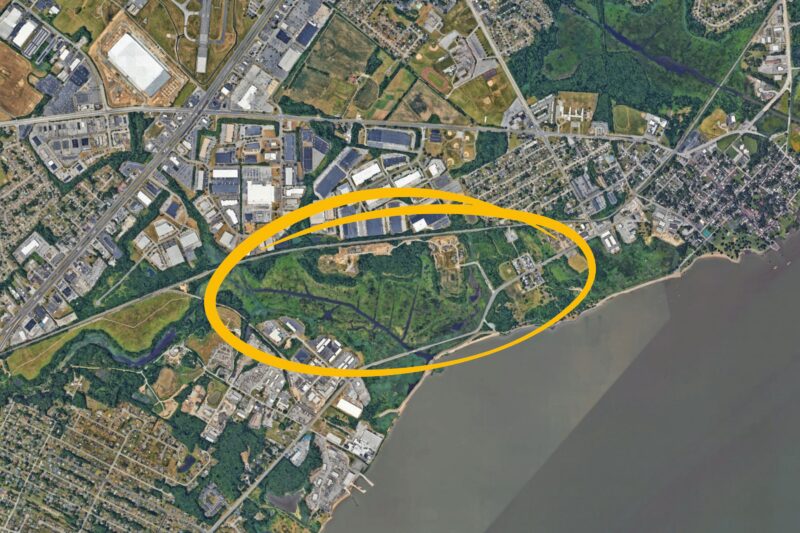 A satellite view of an urban and industrial area with a yellow oval highlighting a section of land near a river or large body of water.
