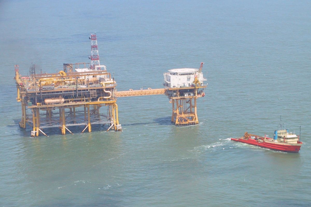 Offshore oil platform with a connected helipad structure in the ocean; a red supply vessel approaches the platform on calm water.