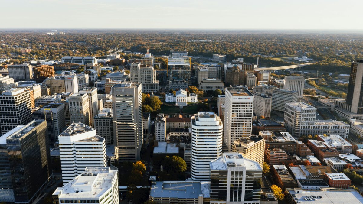 Aerial view of a downtown cityscape with tall office buildings, tree-lined streets, and a prominent historic building at the center.