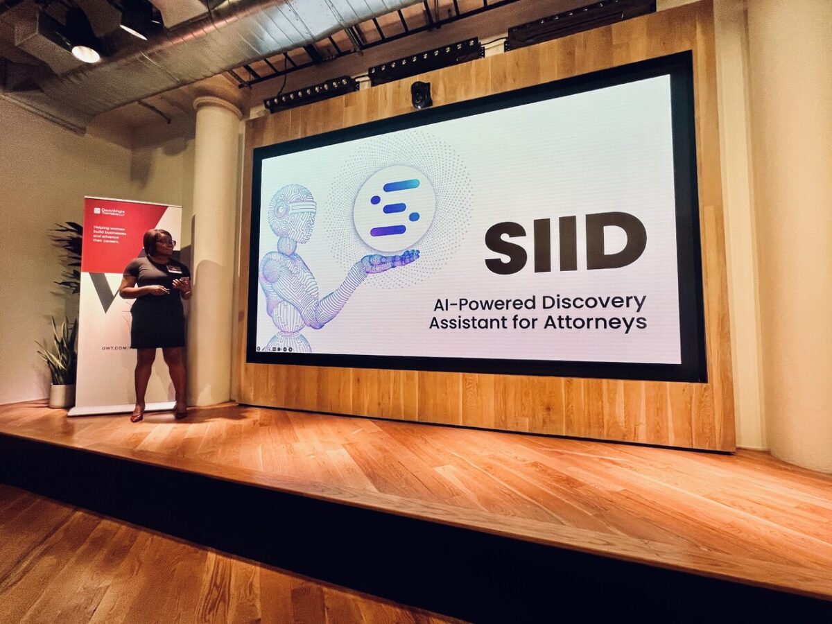 A woman stands on stage next to a large screen displaying "SIID: AI-Powered Discovery Assistant for Attorneys" with a graphic of a robot and circular logo.