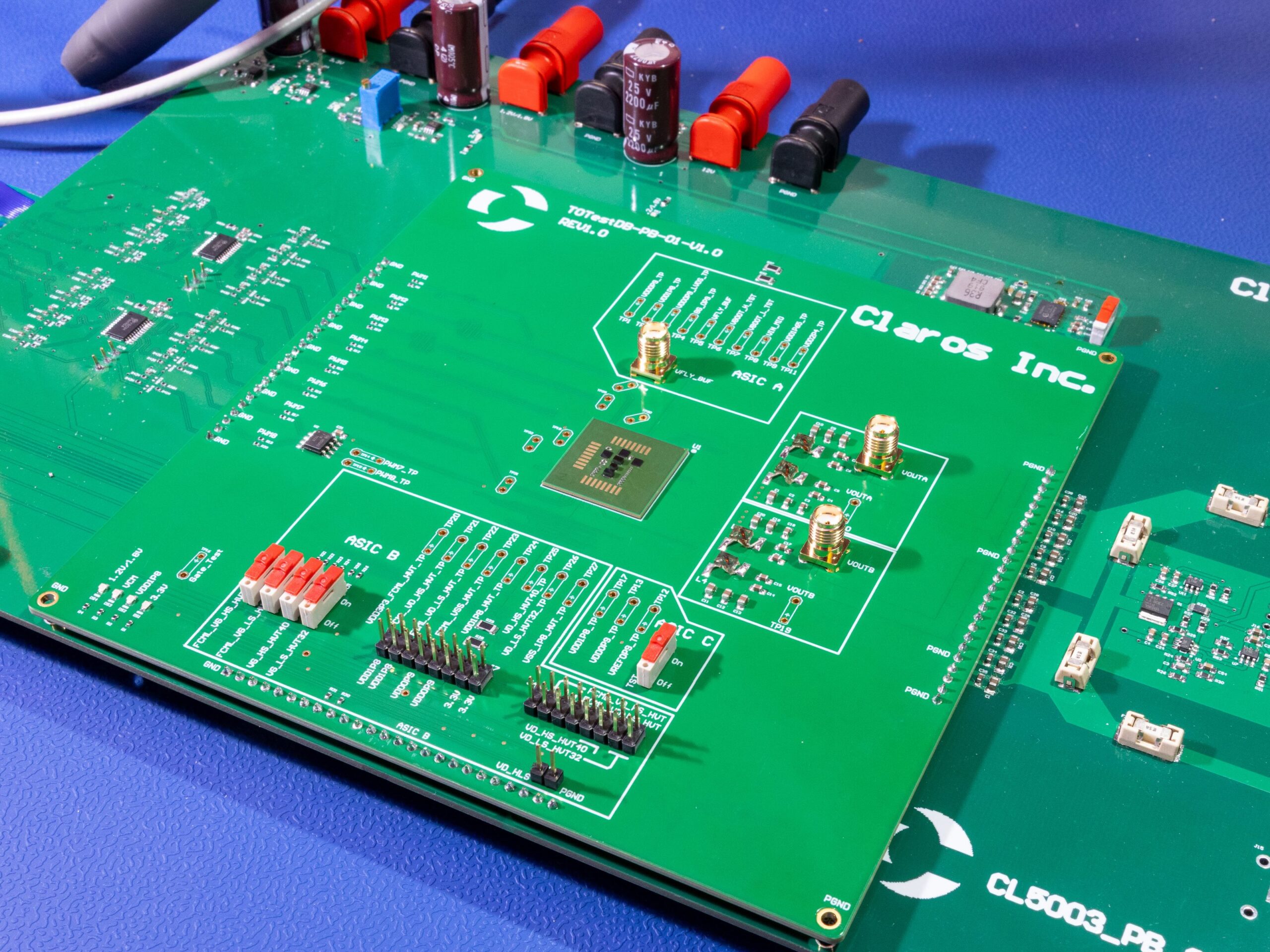 A green printed circuit board labeled "Claros Inc." is mounted on a larger board with various electronic components and connectors on a blue surface.