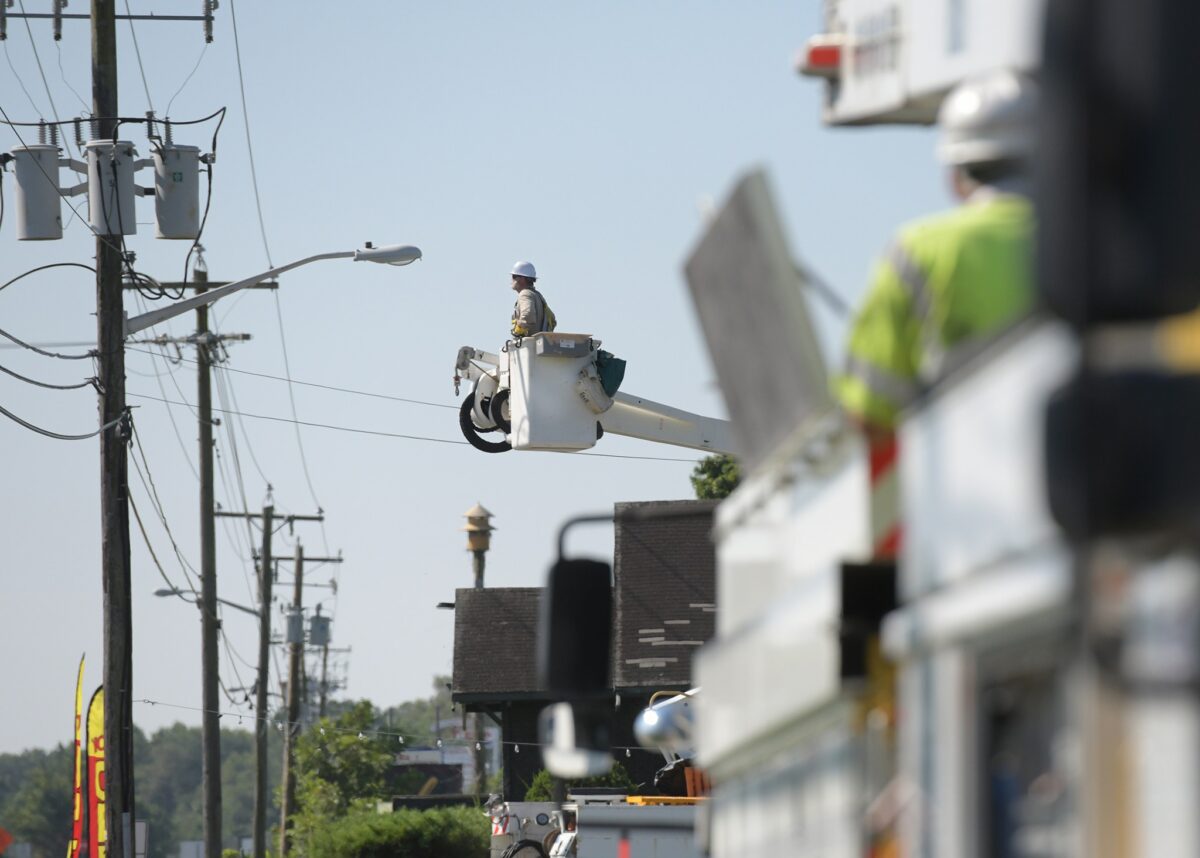 A utility worker in a bucket truck repairs power lines while another worker observes from a separate truck in the foreground.