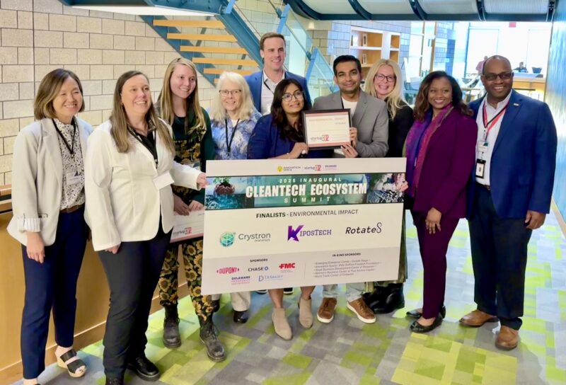 A group of people pose indoors holding a large sign and certificates for the Cleantech Ecosystem Environmental Impact Finalist award.