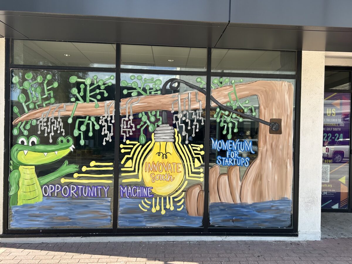 A store window displays a mural with an alligator, a tree branch, a lightbulb labeled "Innovate South," and text reading "Opportunity Machine" and "Momentum for Startups.