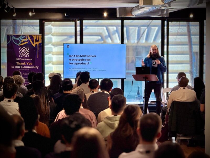 A speaker presents a slide to an audience at a conference. The slide reads, "Isn't an MCP server a strategic risk for a product?!" A banner on the left says, "MCPConference.