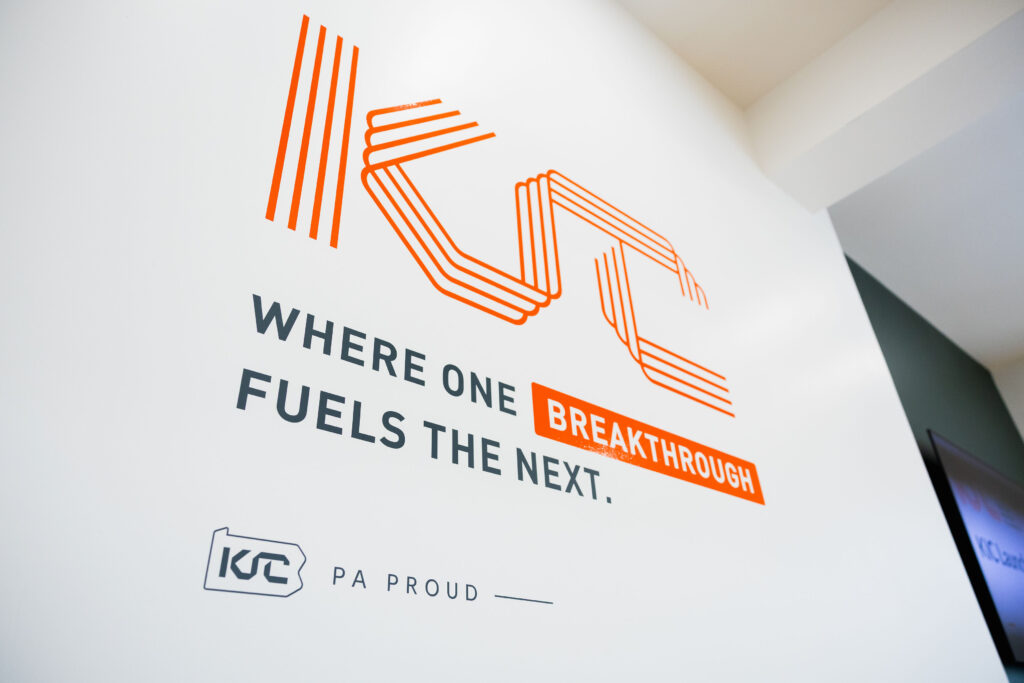 Wall with the KCF Technologies logo and the slogan “Where one breakthrough fuels the next.” The word "breakthrough" is highlighted in orange. "PA Proud" is also displayed.