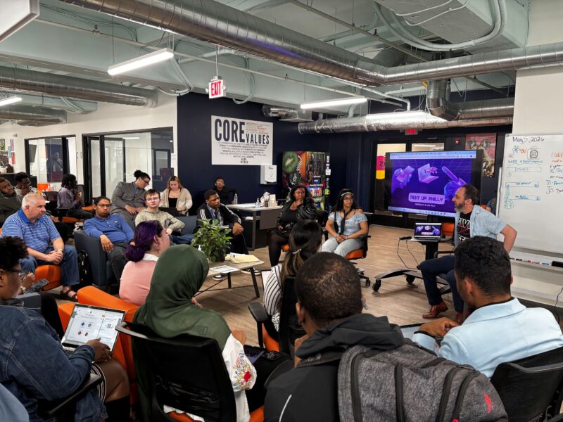 A diverse group of people attends a discussion in a modern office space, with a presentation on a screen and "CORE VALUES" sign on the wall.