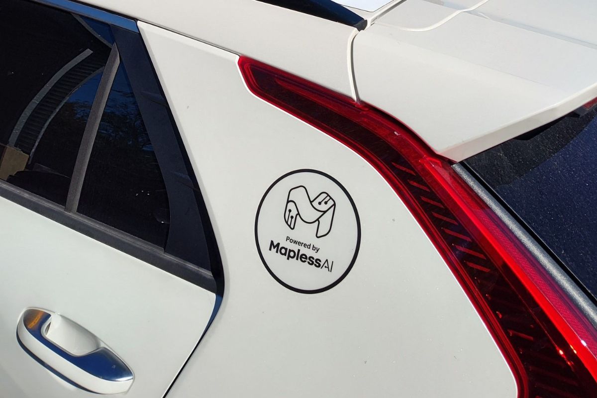A white car with a sticker near the rear window reading "Powered by MaplessAI" and featuring a graphic of two hands shaking.
