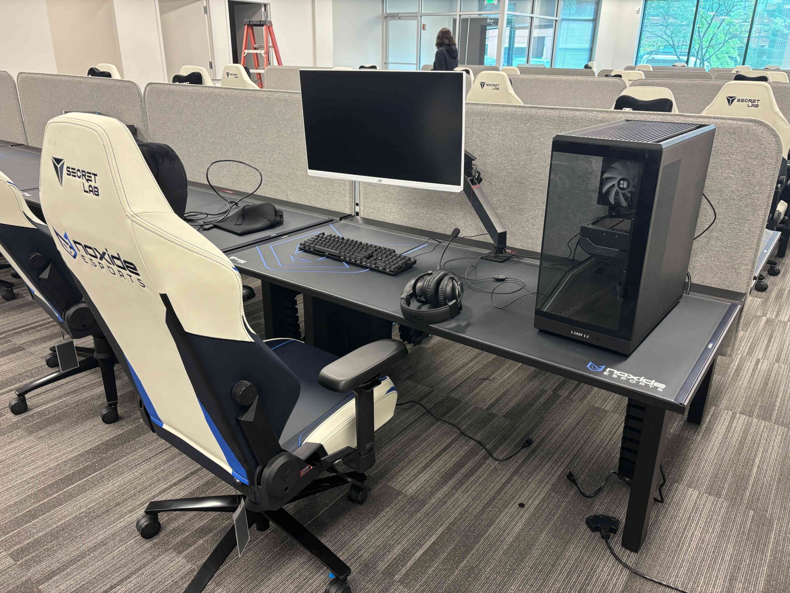 A white gaming chair next to a cubicle setup with a monitor 