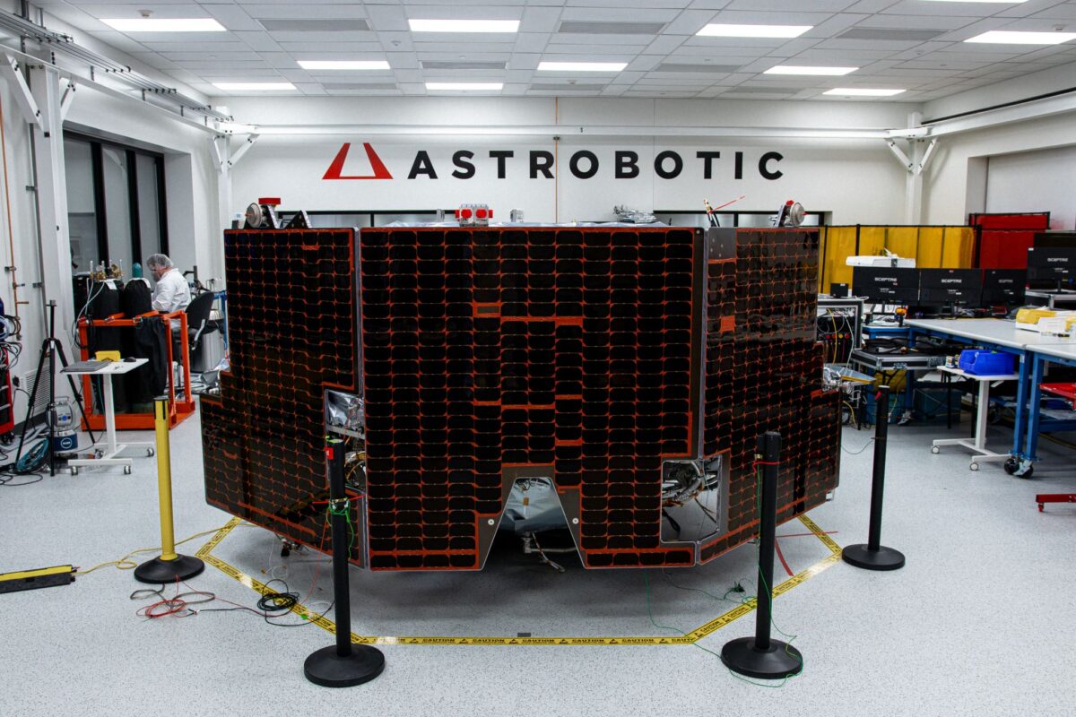 A large spacecraft with solar panels stands in a laboratory under the "Astrobotic" sign, surrounded by equipment and workstations.