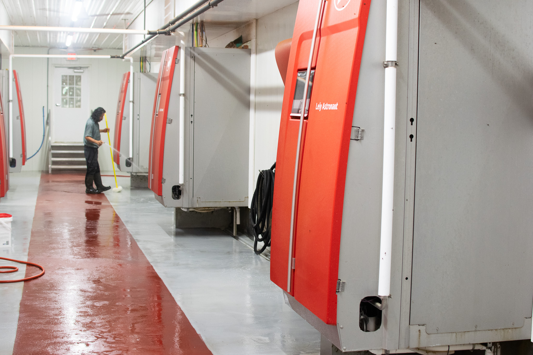 A person hoses down the floor in a clean, brightly lit facility with large red and gray automated machines lined up along the wall.