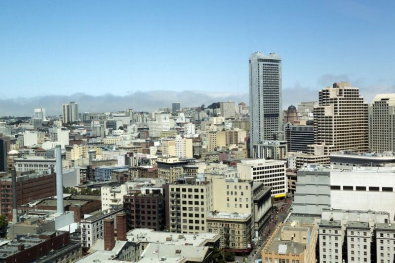 A cityscape view of downtown San Francisco with various high-rise buildings under a clear sky and low clouds in the background.