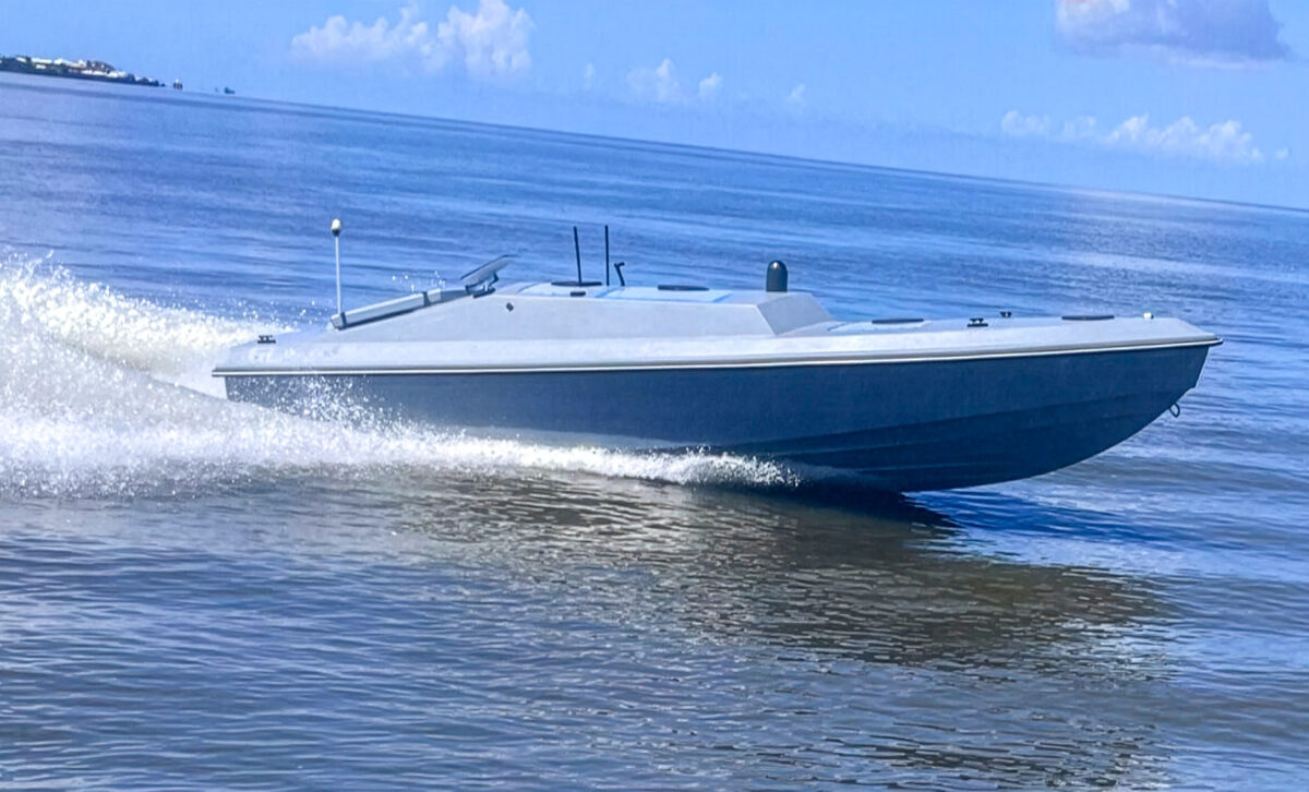 A sleek, gray speedboat moves quickly across calm blue water, leaving a white spray in its wake under a mostly clear sky.