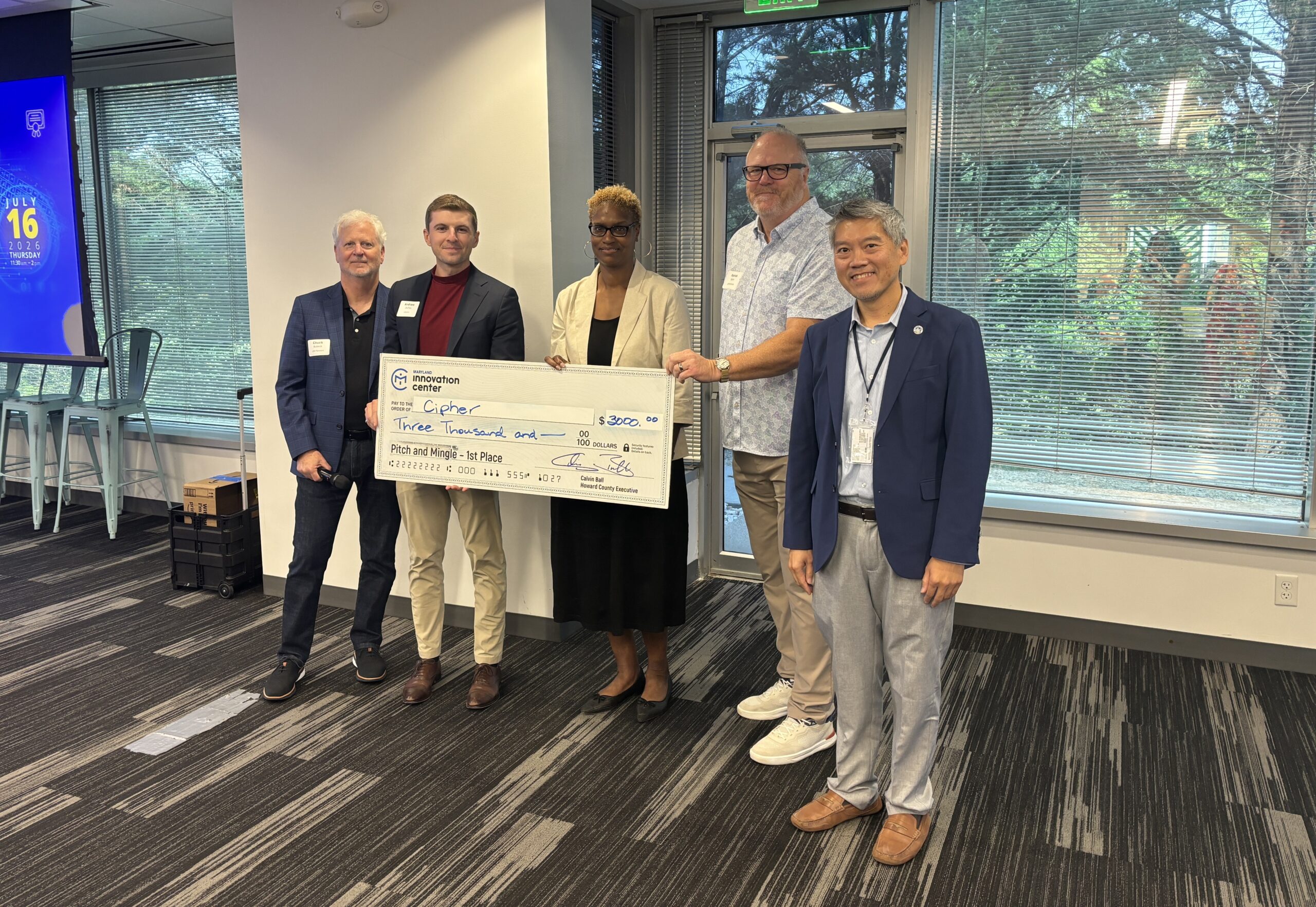 Five people stand indoors holding a large check for $3,000 made out to "Capture" from Walton College’s Office of Entrepreneurship and Innovation.