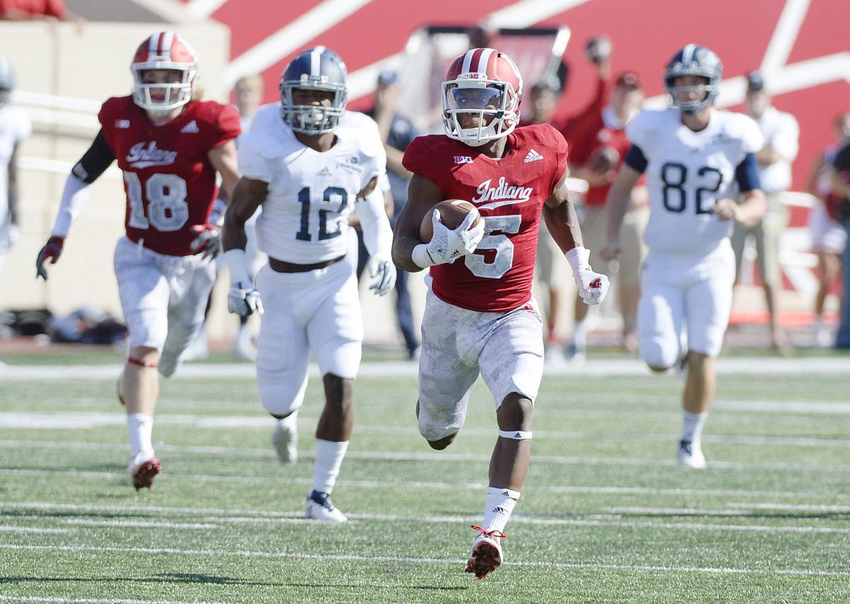 Indiana football player in red runs with the ball down the field as multiple opponents in white uniforms chase him during a game.