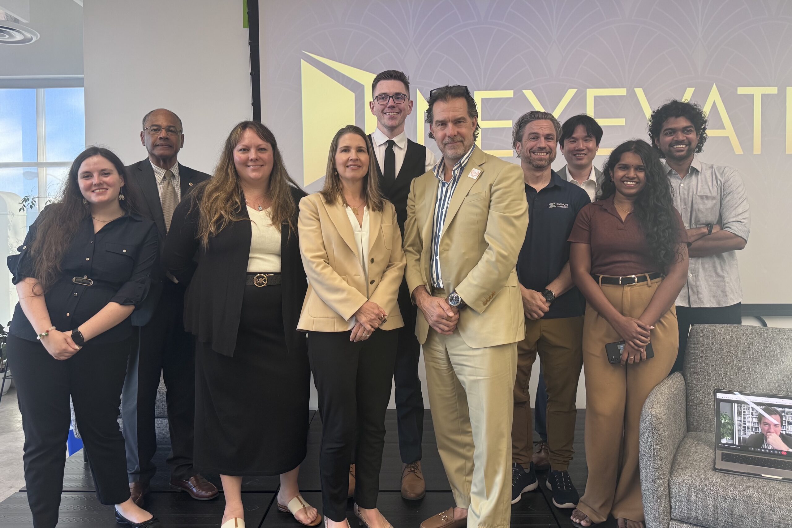 A group of ten people in business attire pose together indoors in front of a screen displaying the word "ELEVATE.