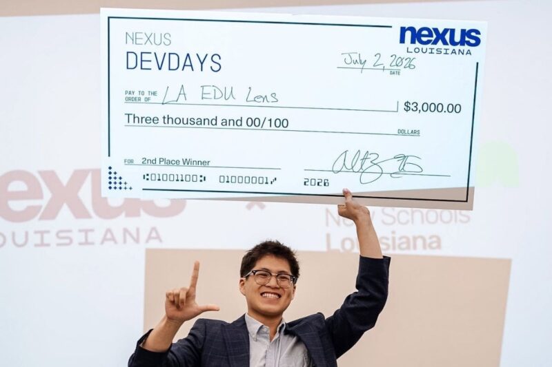 Person holding an oversized $3,000 check for second place from Nexus Louisiana’s DevDays, dated July 2, 2026, awarded to LA EDU Lens, with a smile and an “L” hand gesture.