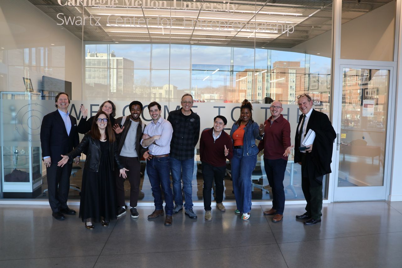 A group of ten people pose and smile for a photo in front of the Carnegie Mellon University Swartz Center for Entrepreneurship entrance.
