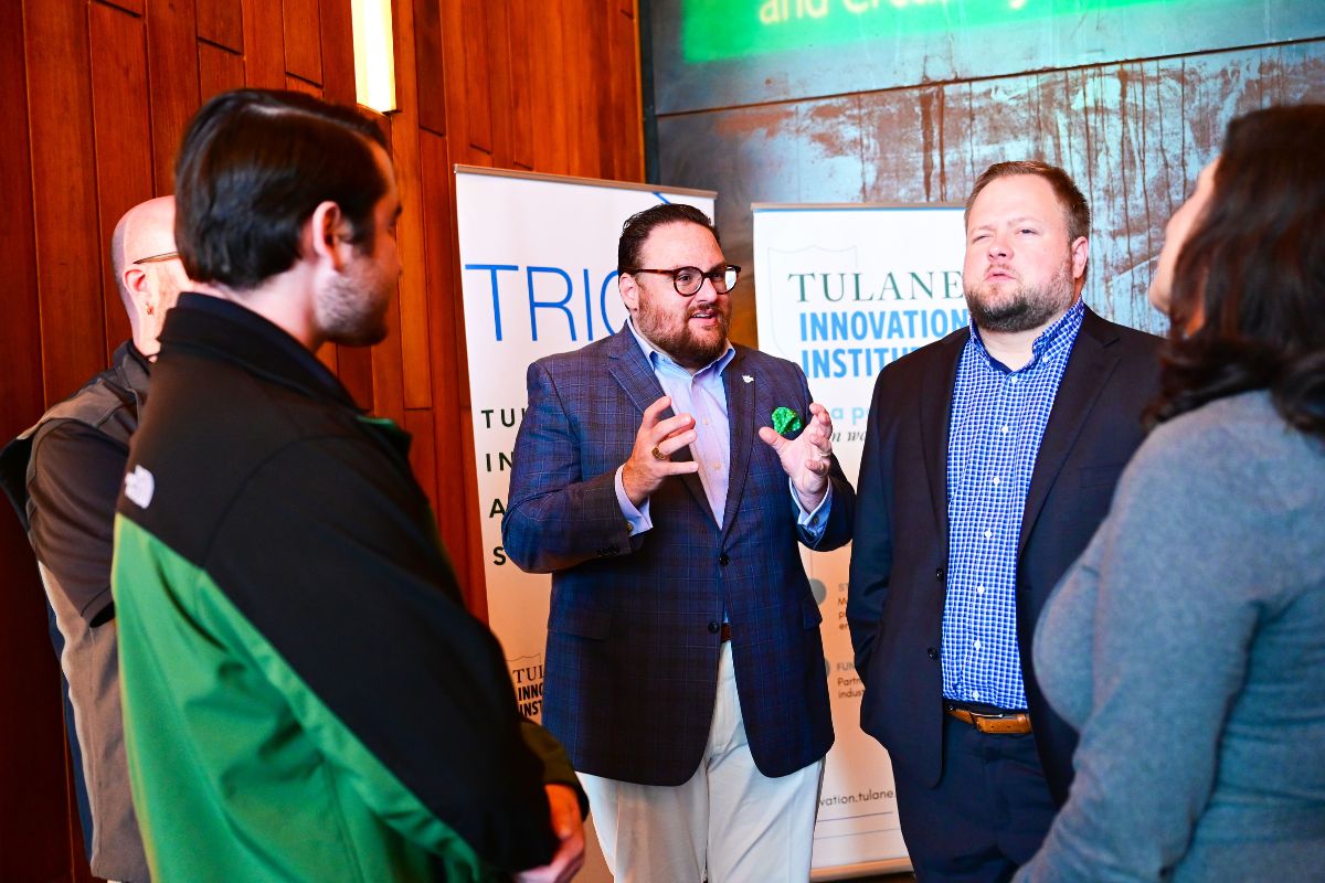 Five people stand in a group having a discussion indoors, with banners for Tulane Innovation Institute visible in the background.