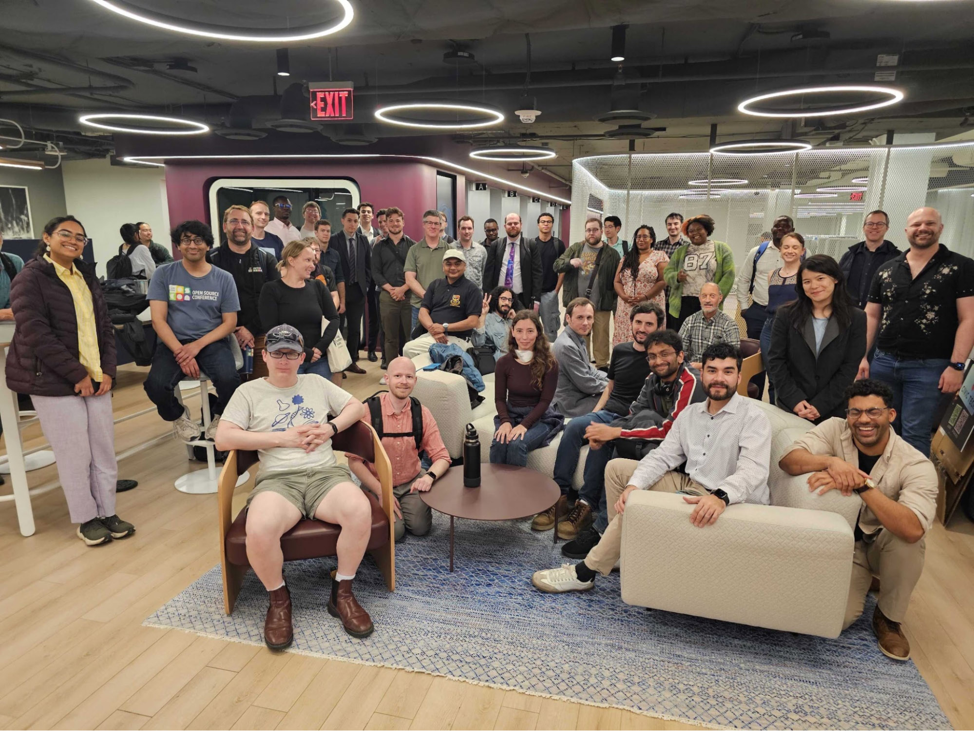 A large group of people pose together in a modern office space with circular ceiling lights and comfortable seating.