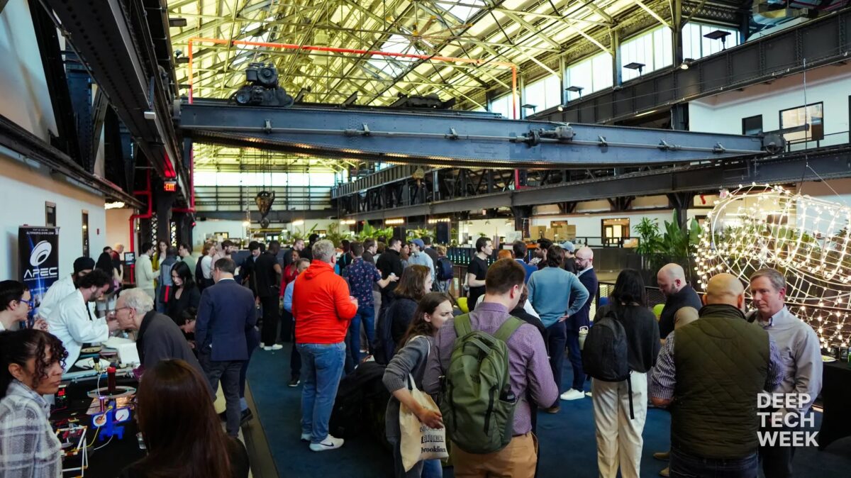 A large group of people gathers at an indoor tech event with booths, a high glass ceiling, and “Deep Tech Week” text visible in the corner.