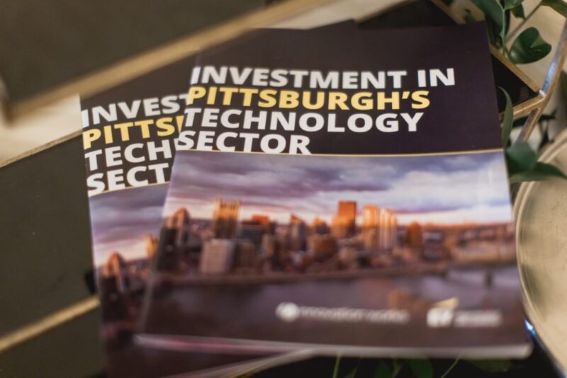 Two booklets titled “Investment in Pittsburgh’s Technology Sector” with a cityscape image on the cover are stacked on a reflective surface.