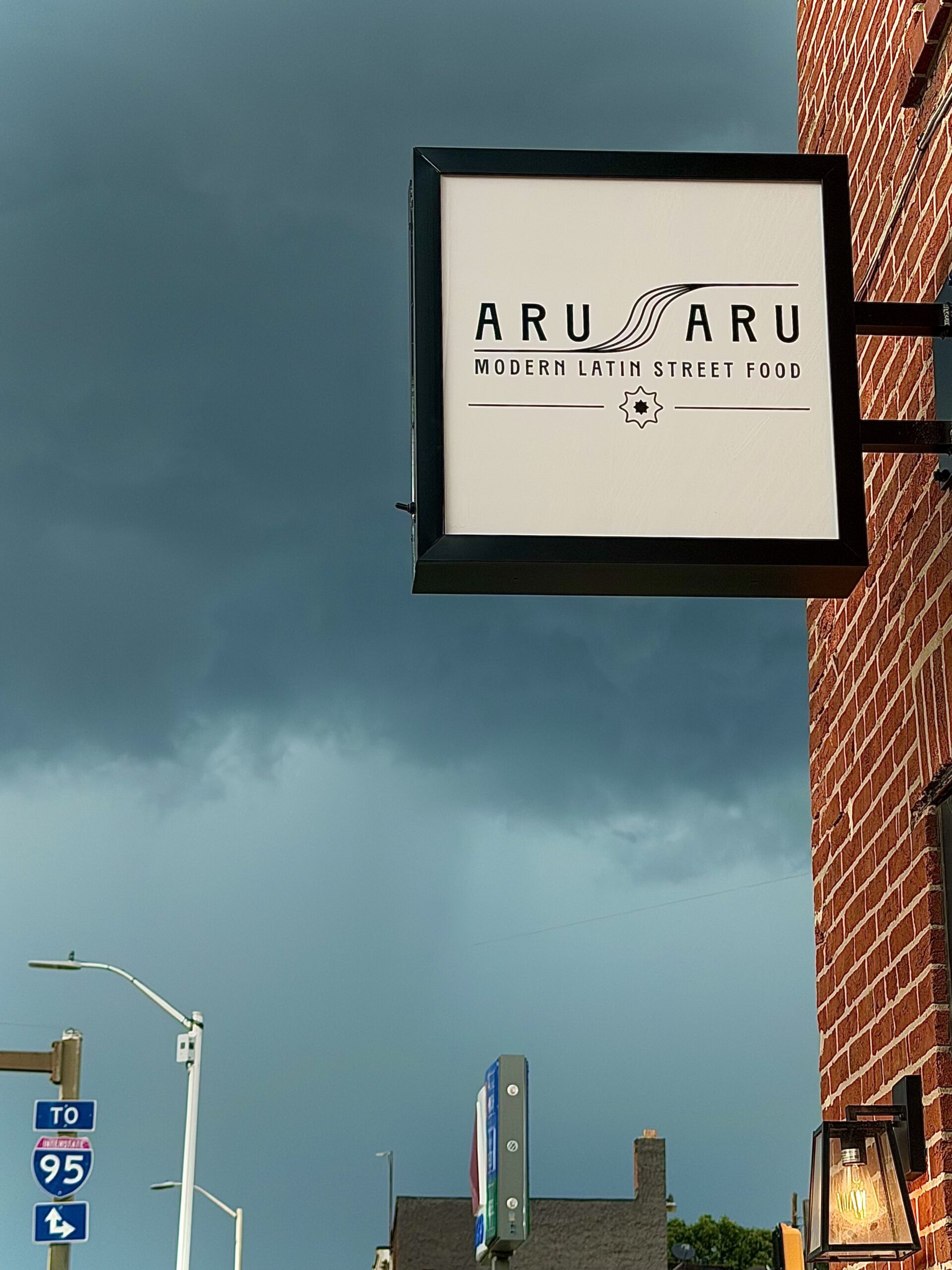 A restaurant sign reads “ARU SARU Modern Latin Street Food” against a cloudy sky, with a nearby I-95 highway sign visible in the background.