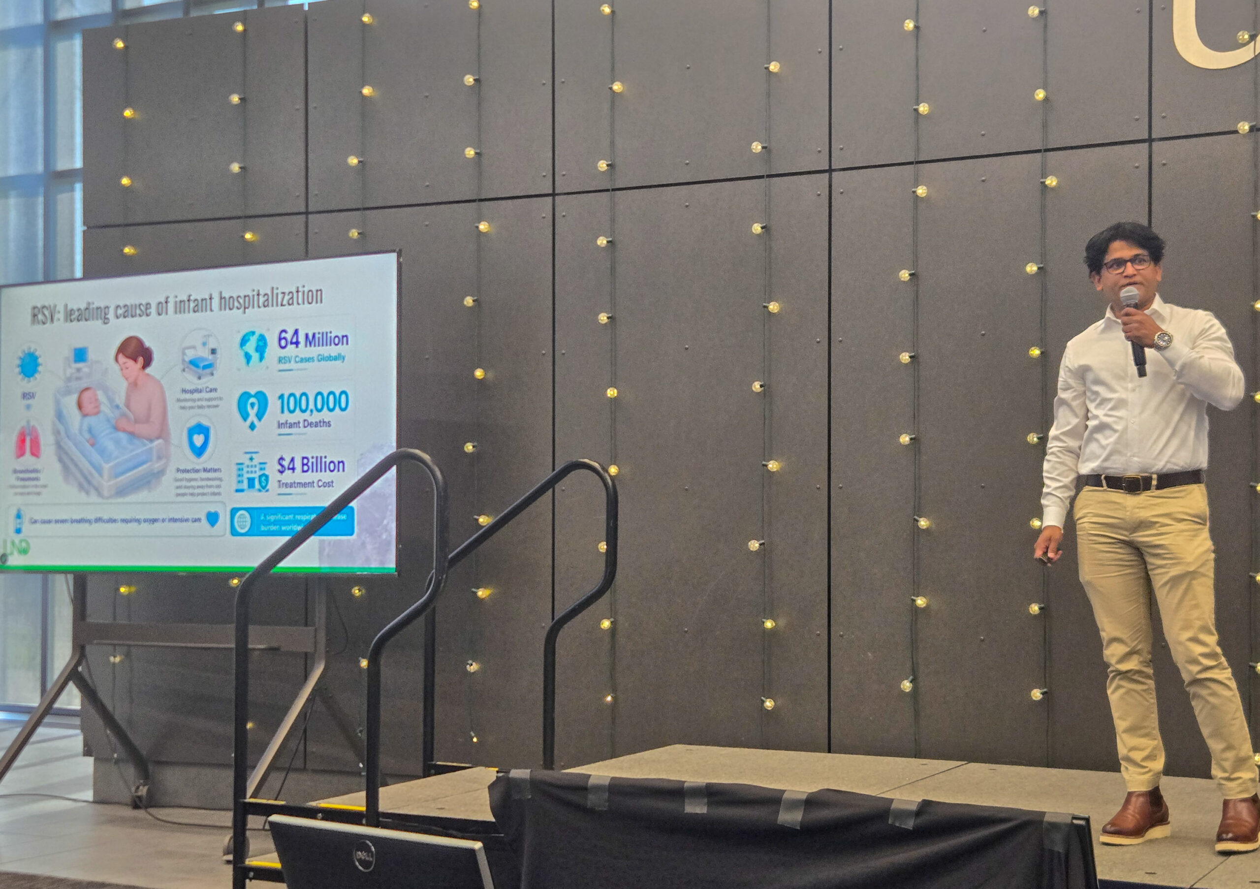 A man stands on stage presenting a slide about RSV and infant hospitalization, showing statistics and illustrations, with a microphone in hand.