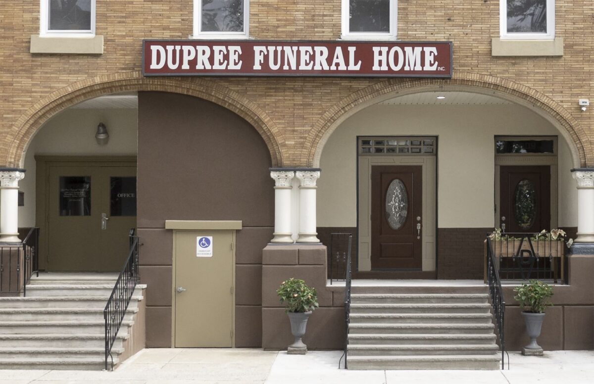 The entrance of Dupree Funeral Home with two stairways, a brown double door, a tan door, and a red and white sign above the arches.