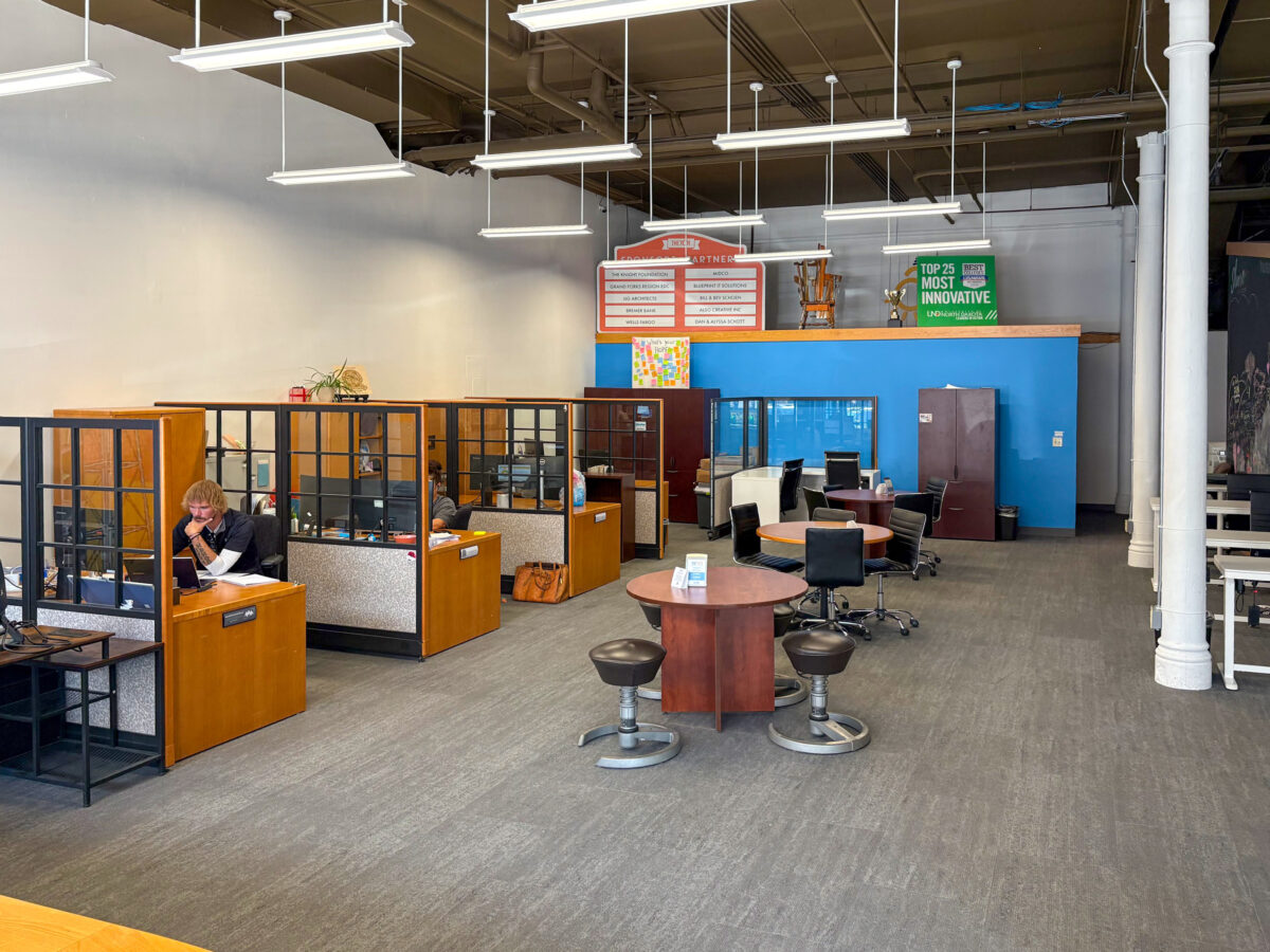Open office space with cubicles, desks, and chairs; one person working at a desk; informational signs and colorful artwork on the walls; modern, corporate environment.