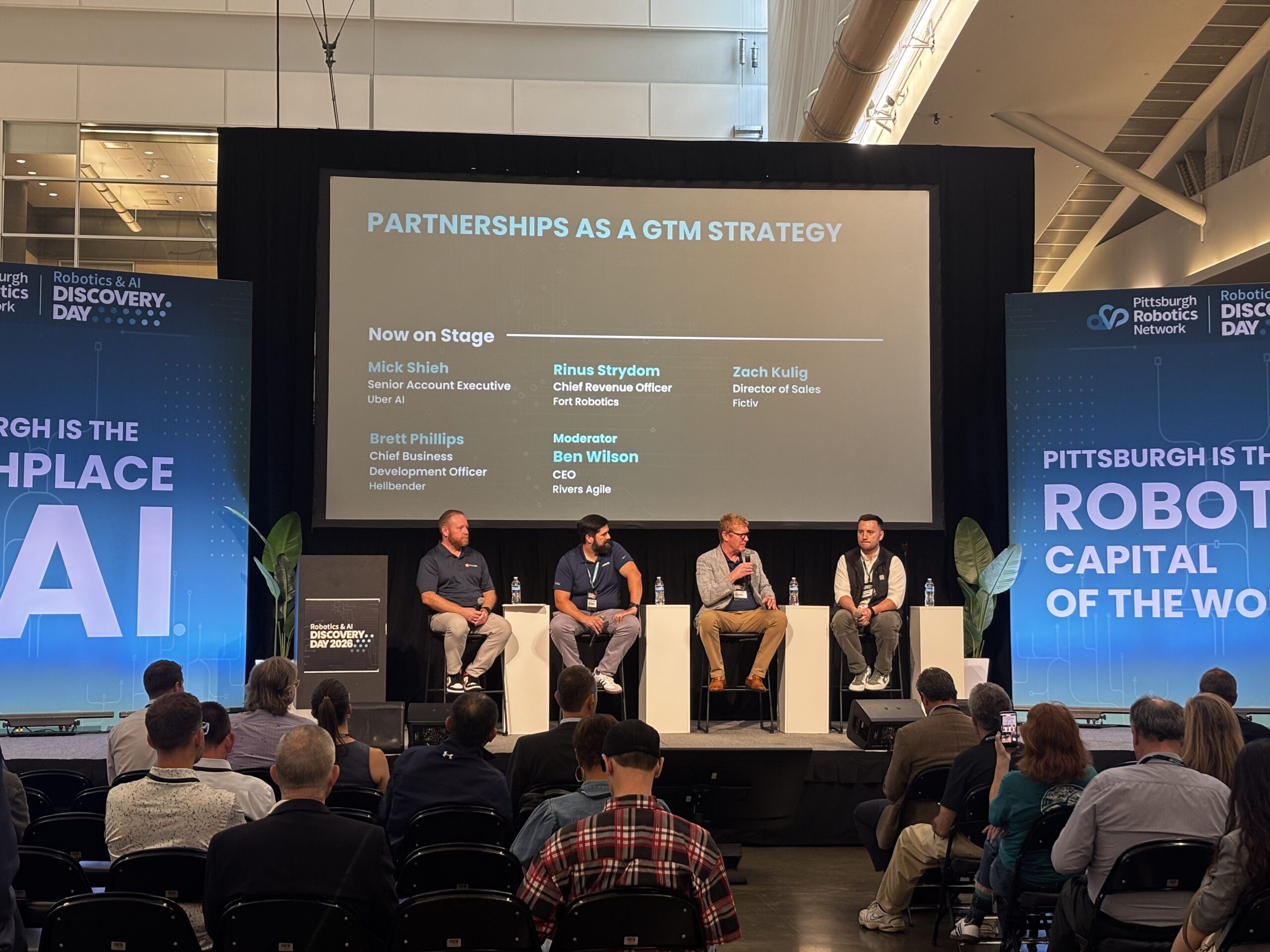 Four panelists and a moderator discuss “Partnerships as a GTM Strategy” on stage at a robotics conference, with seated audience members watching.