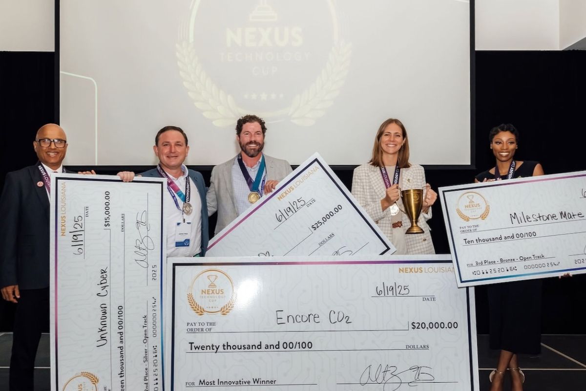 Five people stand on stage holding oversized checks and a trophy in front of a Nexus Technology Cup screen; the checks display awards for innovation and milestone achievements.