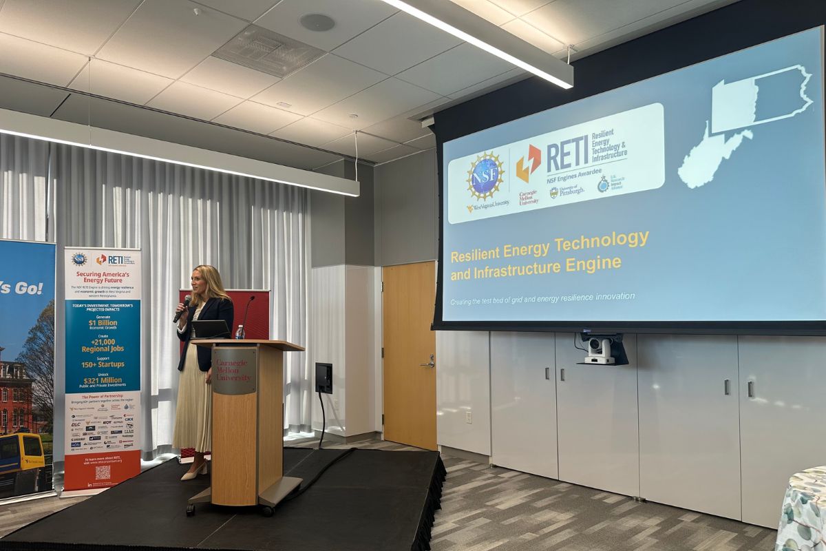 A woman stands at a podium giving a presentation on “Resilient Energy Technology and Infrastructure Engine” in a conference room with a large projection screen.